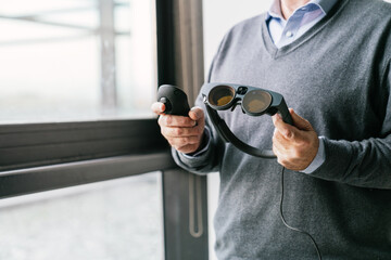 A close-up of an older businessman holding a VR headset and controller, symbolizing technological...