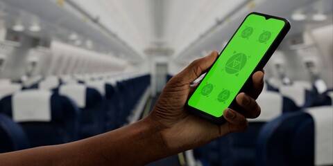 Hand holding a phone with a green screen against an airplane cabin backdrop