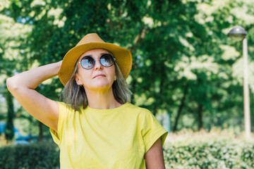 Portrait of a young woman in a summer park, straw hat with brim, sunglasses, yellow T-shirt.