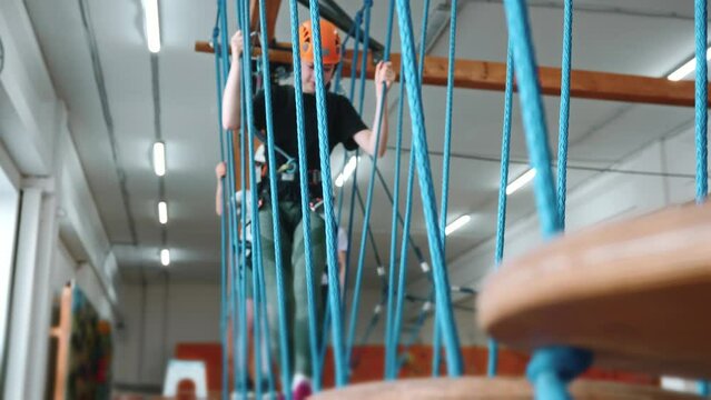A view through the ropes, a 13-year-old girl passes an obstacle course in a rope park in protective gear. A brave and strong little girl walks through the wobbly grounds. High quality 4k footage