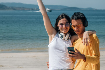 young couple with headphones and phone on the beach having fun
