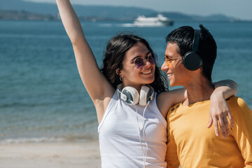 young couple with headphones and phone on the beach having fun