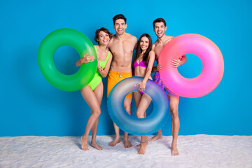 Full length photo of charming cute fellows company wear swimsuits going swim circles isolated blue color background