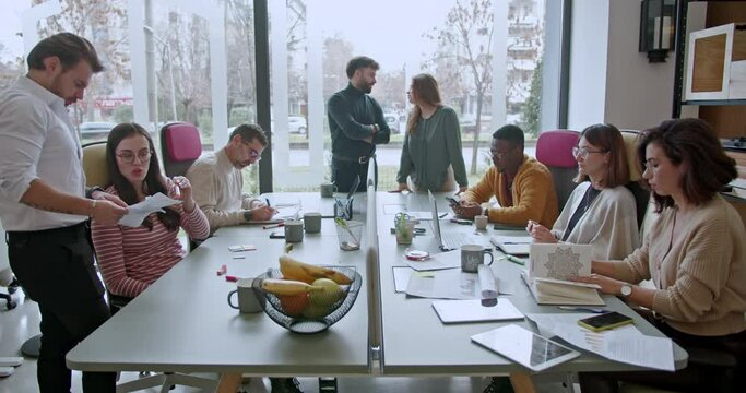 At a busy office table, a group of diverse employees engages in brainstorming and problem-solving. Men and women discuss ideas and collaborate on tasks, showcasing teamwork and innovative thinking.