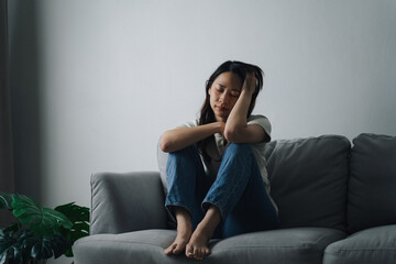 Obraz premium Unhappy lonely depressed woman is sitting on the couch and holding her head.