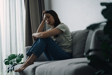 Unhappy lonely depressed woman is sitting on the couch and holding her head.