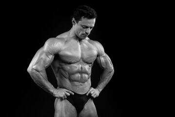 Fototapeta premium Athlete bodybuilder posing for a sports magazine in the studio on a black background. Grain effect used