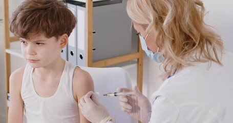 Vaccination, pediatrician wearing uniform, stethoscope vaccinating little cute boy in hospital, doctor making prick, injection to brave smiling preschool child in clinic, children healthcare concept 