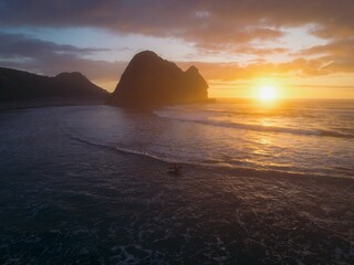 Surfer exiting the water at sunset. Lion rock is in the background. Piha, Auckland, Auckland, New Zealand.