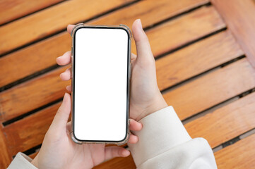 Top view image of a woman's hand holding a white-screen smartphone mockup over a wooden table.