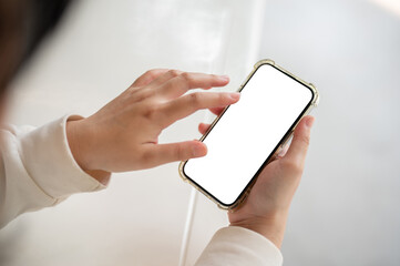 A woman in a white sweater holding a smartphone white-screen mockup over a white table indoors.