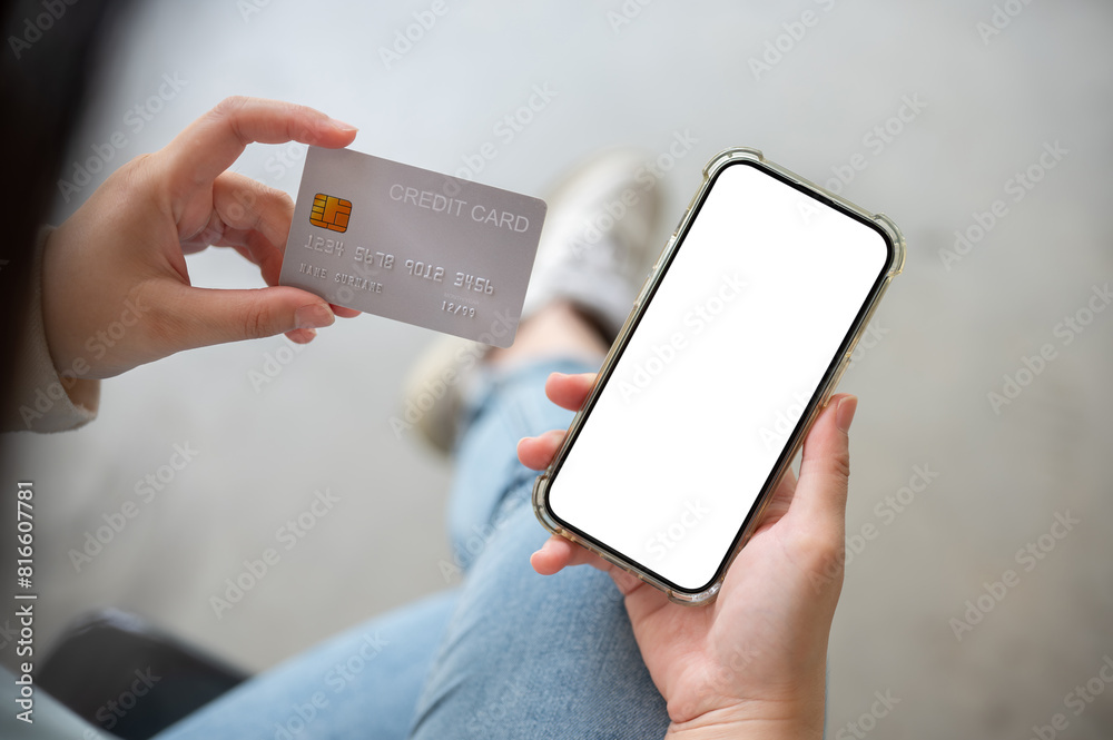 Wall mural a close-up image of a woman holding a credit card and a smartphone, sitting indoors. online shopping