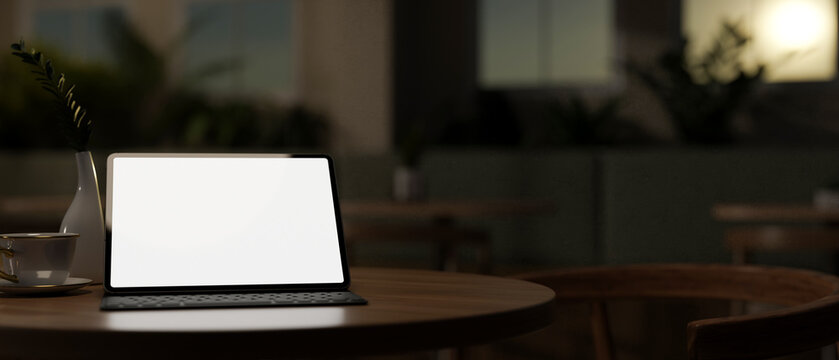 A close-up image of a digital tablet mockup on a wooden table in a dark room in the evening. - Powered by Adobe