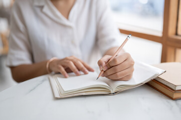 A cropped shot of a woman writing something in her notebook while sitting in a coffee shop.