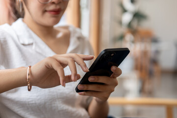 A close-up image of an Asian woman sitting on the sofa in the living room, using her smartphone.
