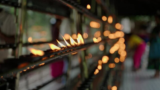 Devotees oil lamps in Buddhist rituals. Flames flicker, create tranquil ambience. Worshippers in colorful attire perform religious practices, pray. Cultural ceremony, tradition spiritual site. Slowmo