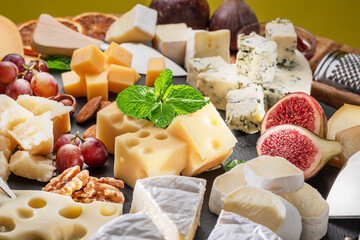 Variety of sliced cheeses with fruits, mint, nuts and cheese cutting knives.