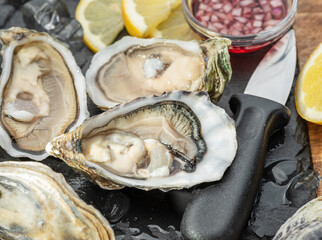 Opened raw oysters with sauce and lemon slices on gray stone serving board. Delicacy food. © volff