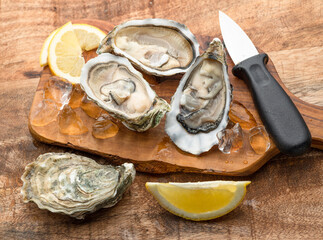 Three opened raw oysters and oyster knife on wooden table. Top view.