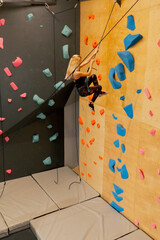at the climbing wall young girl goes down the safety rope, the coach insures against falling