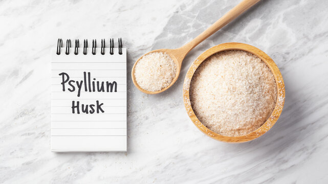 Psyllium husk in wooden bowl and spoon with psyllium husk word on notebook on marble table