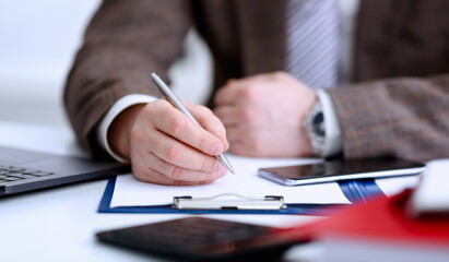 Male arm in suit and tie hold silver pen filling schedule in notepad at office workplace closeup....
