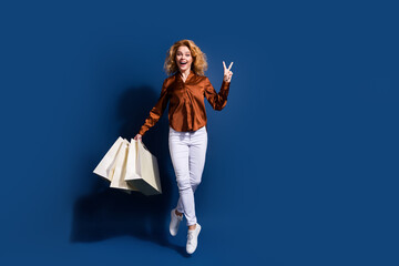 Full length photo of positive woman dressed silk shirt hold shopping bags fly showing v-sign...