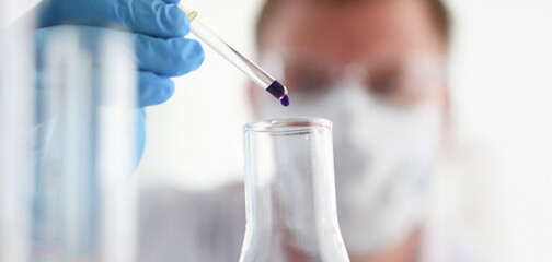 A male chemist holds test tube of glass in his hand overflows a liquid solution of potassium permanganate conducts an analysis of water samples versions of reagents using chemical manufacturing.