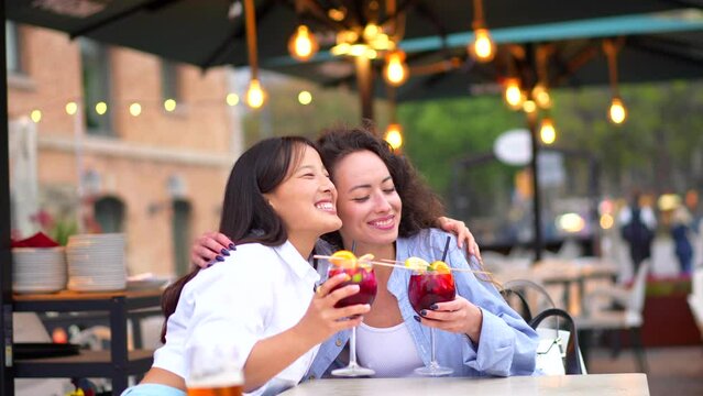 Lesbian multiracial couple toasting with cocktails sitting in an outdoor terrace in the city