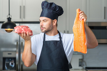 Handsome man cooking fish and meat, salmon and beef in kitchen. Portrait of casual man cooking in the kitchen with fish and meat ingredients. Casual man preparing raw fish and meat in kitchen.