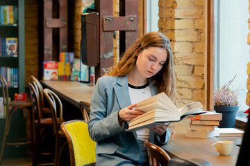 in bookstore near the window a beautiful student is sitting reading books preparing for exams