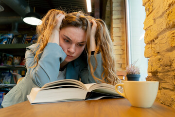 close up in bookstore near window a beautiful student is sitting boring reading books preparing for...