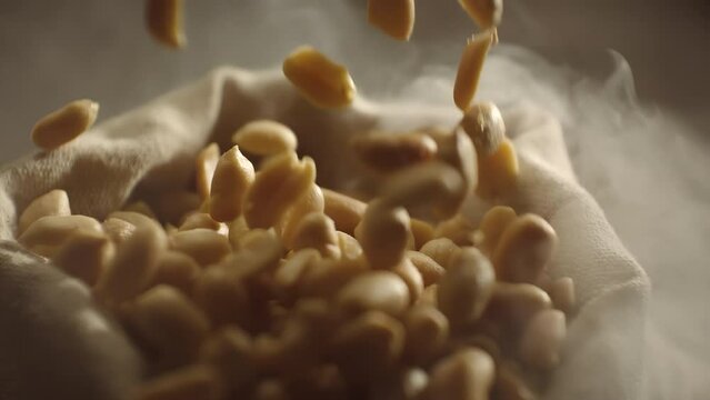 Crispy roasted salted peanuts falling in super slow motion close up. Hot delicious fried peanuts snacks with smoke flying. High speed 1000 fps footage
