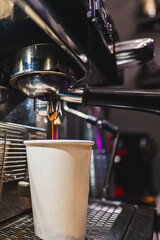 close-up of an espresso machine dispensing coffee into a white paper cup.