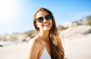 Portrait, beach and woman with sunglasses, excited and smile with happiness, holiday and weekend break. Face, person and girl with eyewear, seaside and vacation with getaway trip, travel and sunshine