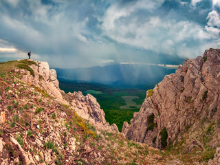 Tourist on the edge of cliff. Summer rain in Crimea Mountains. Amazing morning scene of highland. Beauty of nature concept background.