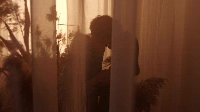 A silhouetted couple shares a romantic kiss behind sheer curtains, capturing a moment of love and intimacy. The dimly lit room adds a soft, romantic glow. Slow Motion. 