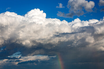 Huge white storm clouds with a vibrant rainbow below