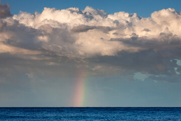 Beautiful vibrant rainbow descending from the clouds to a blue ocean