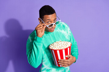 Photo of suspicious guy wear teal sweatshirt enjoy film eat pop corn look you isolated purple color...