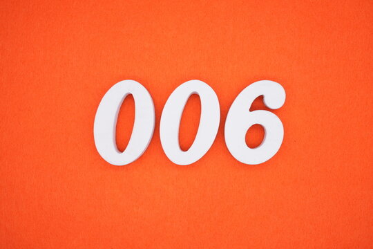 The number 006 is made from white painted wood placed on a background of orange paper.