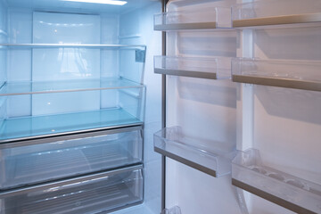 Background texture of a clean and empty fridge with multi-level shelf compartments and lights on and doors open.