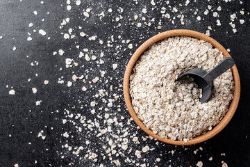 Rolled oats, healthy breakfast cereal oat flakes on black slate background. Top view. Copy space