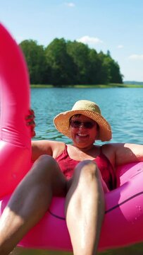 Elderly woman floating on inflatable flamingo and unicorn. Funny active pensioner enjoying summer vacation on the beach in Europe. A vertical video.