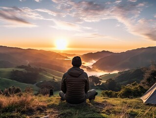 a man sitting on a hilltop watching the sunrise over a beautiful mountain landscape.