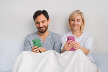 Couple lying in bed browsing internet read text message on modern cellphone cell phone cellular....