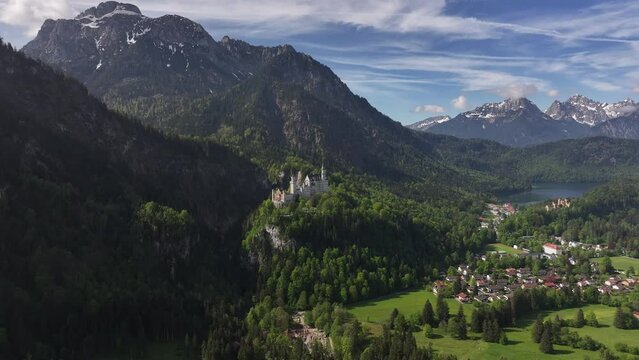 Neuschwanstein castle nestled in the bavarian alps, surrounded by lush greenery and a small village, aerial view