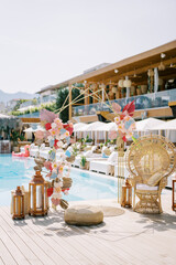 Colorful wedding arch stands near a wicker chair on the shore of the pool