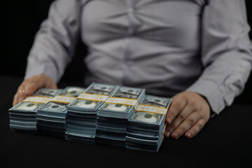 Stacks of hundred dollar bills on a black background in front of a man in a business shirt....