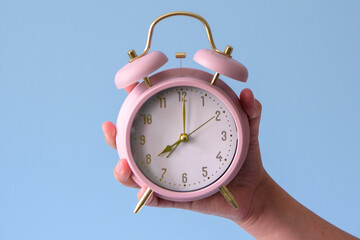 Girl holding a pink alarm clock that is set to the time of 8:00. The clock is on a blue background